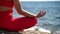 A young woman in red sportswear relaxes while practicing yoga on the beach by the calm sea, close-up of hands, gyan