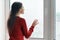 Young woman in red sweater looking out the window, female put her hands on the window glass, side view, window in skyscraper in