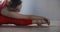 Young woman in red tracksuit sitting on the yoga mat and leaning forward to her feet, person does physical training