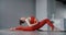 Young woman in red training wear sitting on the yoga mat and leaning forward to her feet, person does physical training