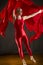 Young woman in red unitard swirling red fabric in studio.