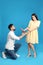 Young woman rejecting engagement ring from boyfriend on blue background