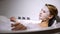 Young woman relaxing in bath with foam bubbles, natural essence mask on face