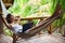 Young woman relaxing in a hammock with laptop in a tropical resort.