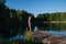 Young woman relaxing by the lake at sunset, harms outstretched. Doing youga in the morning at forest lake.