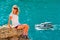Young Woman relaxing on rocky cliff with blue Sea and Ship yacht on background