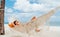 Young woman relaxing in wicker hammock on the sandy beach on Mauritius coast and enjoying wide ocean view waves. Exotic countries