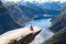 Young woman relaxon Trolltunga. Happy girl enjoy beautiful lake and good weather in Norway.