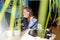 Young woman remote working or studying on computer in front of monitor in home. Blurred green palm leaves in foreground