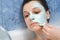 Young woman is removing alginate mask from her face lying in bathroom with foam.