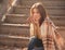 Young woman resting and drinking tea sitting in autumn garden on the steps, wrapped in a woolen plaid blanket.