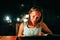 Young woman resting in an outdoor cafe looks menu at the sea on beautiful bokeh lights