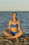 Young woman rests on the beach on a hot summer day. Young attractive smiling woman practicing yoga on a sea. Healthy active
