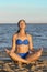 Young woman rests on the beach on a hot summer day. Young attractive smiling woman practicing yoga on a sea. Healthy active