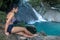 A young woman in retro swimsuit resting on the shore of the waterfall