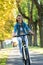 Young woman ride bike in autumn park. Enjoying while cycling in nature during autumn day