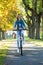 Young woman ride bike in autumn park. Enjoying while cycling in nature during autumn day