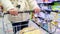 A young woman rolls a shopping basket between rows of goods. Supermarket products, household goods.