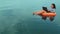 A young woman in an rubber ring swims near the sea in the morning and works in a laptop.