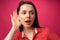 Young woman's reaction on what she heard, surprise, on pink background