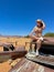 Young woman in safari overalls sits on the rooftop of abandoned old rusty car.