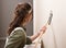 Young woman is sanding wall with pole sander before painting