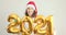 Young woman in Santa Claus hat dancing and having fun holding in hand numbers 2021. Girl in Christmas hat and dancing in