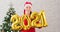Young woman in Santa Claus hat dancing and having fun holding in hand numbers 2021. Girl in Christmas hat and dancing