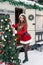 Young woman in santa costume decorates the Christmas tree at winter campsite