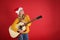 Young woman in Santa hat acoustic guitar on red background, space for text. Christmas music