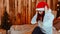 Young woman in santa hat and glasses preening herself in front of camera. Pretty female sitting on bed and adjusting