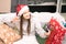 A young woman in Santa hat at home congratulates friends on Christmas and new year via smartphone, shows gifts
