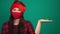 Young woman in santa hat and medical red mask holds invisible object, keeps palm raised