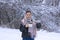 Young woman in scarf on her head in winter in the forest pours hot tea into mug from thermos. Portrait on background of trees in