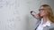 Young woman scientist writes formulas on a white board.