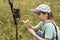 Young woman scientist zoologist writing down data from trap camera to notepad, observing wild animals in reserve taiga forest,