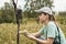 Young woman scientist zoologist writing down data from trap camera to notepad, observing wild animals in reserve taiga forest,