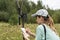 Young woman scientist zoologist writing down data from trap camera to notepad, observing wild animals in reserve taiga forest,