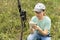 Young woman scientist zoologist writing down data from trap camera to notepad, observing wild animals in taiga forest, monitoring