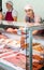 Young woman seller lays out sausages in butcher shop