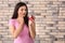 Young woman with sensitive teeth and apple on brick wall background