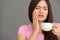 Young woman with sensitive teeth and cup of hot coffee on grey background