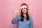 Young woman shapes little gesture, demonstrates something very tiny, wears winter sweater and Christmas red hat