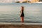 A young woman in a short dress stands on the beach at sunset