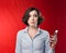 A young woman with a short haircut in a blue office blouse on a red background holding a telephone in hand