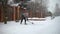 A young woman shovels snow in front of a private house on a winter evening