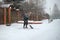 A young woman shovels snow in front of a private house on a winter evening