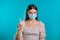 Young woman showing no finger, stop gesture. Girl in face medical mask during coronavirus pandemic. Portrait on blue