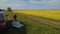 Young woman sit on roadside near her car and enjoy beautiful canola flower field