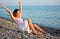 Young woman sits ashore of sea with rised hands